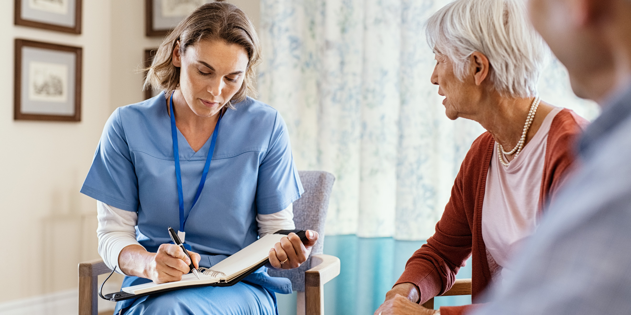 A nurse is sitting in a chair and talking to an elderly woman.