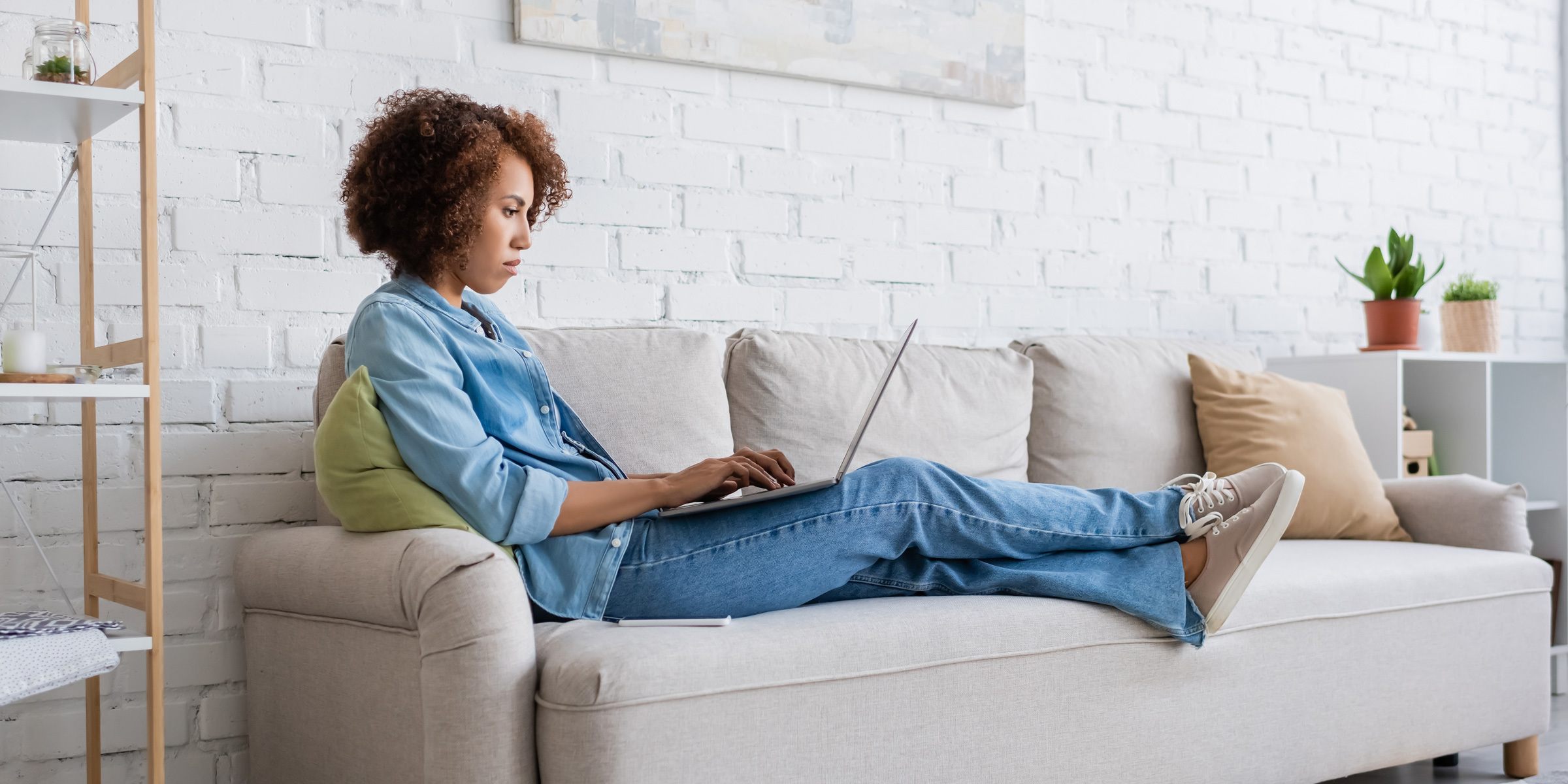 Woman laying upright on a sofa while browsing on a laptop