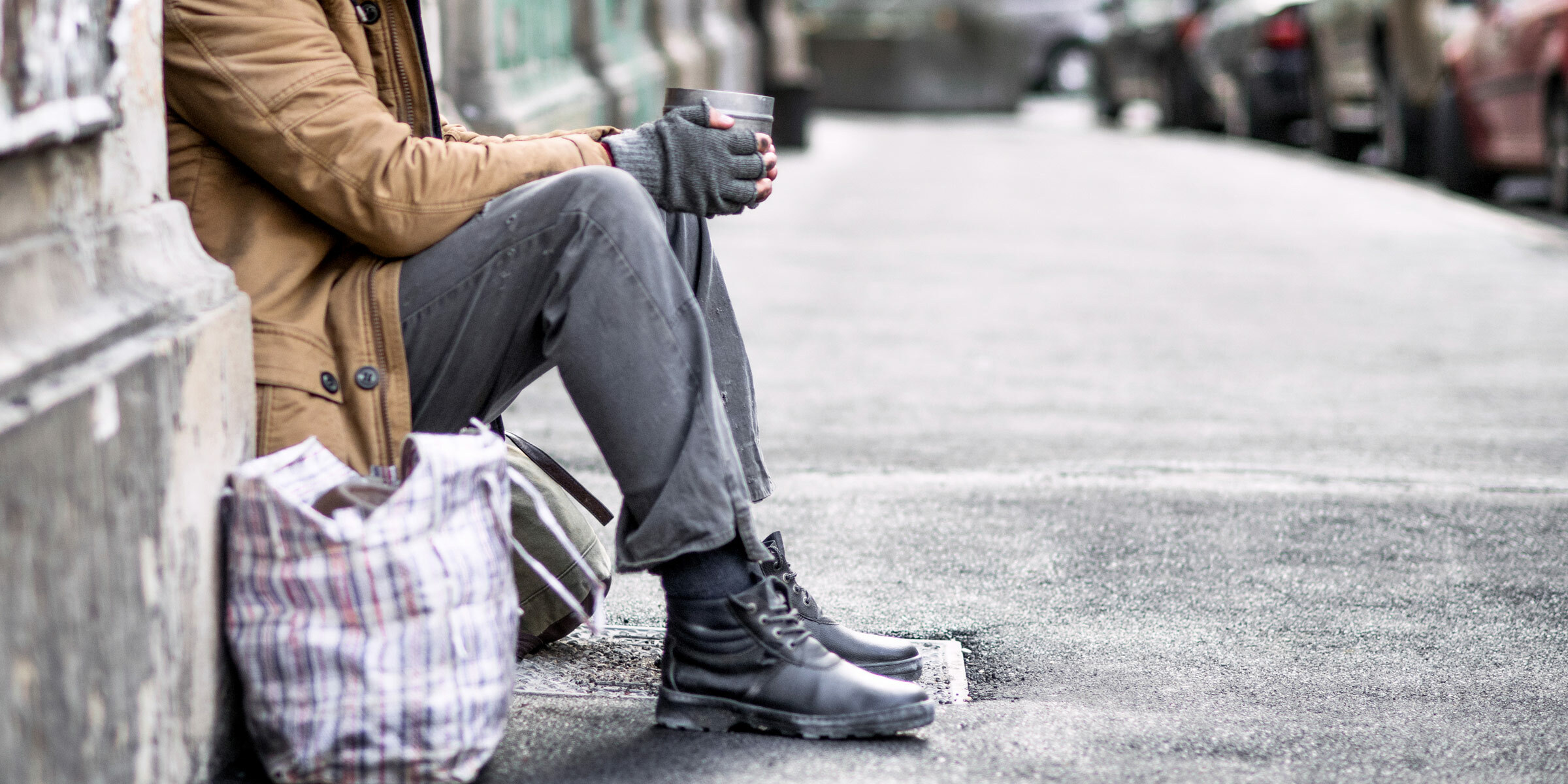 Homeless man sitting on the sidewalk holding a can for money.