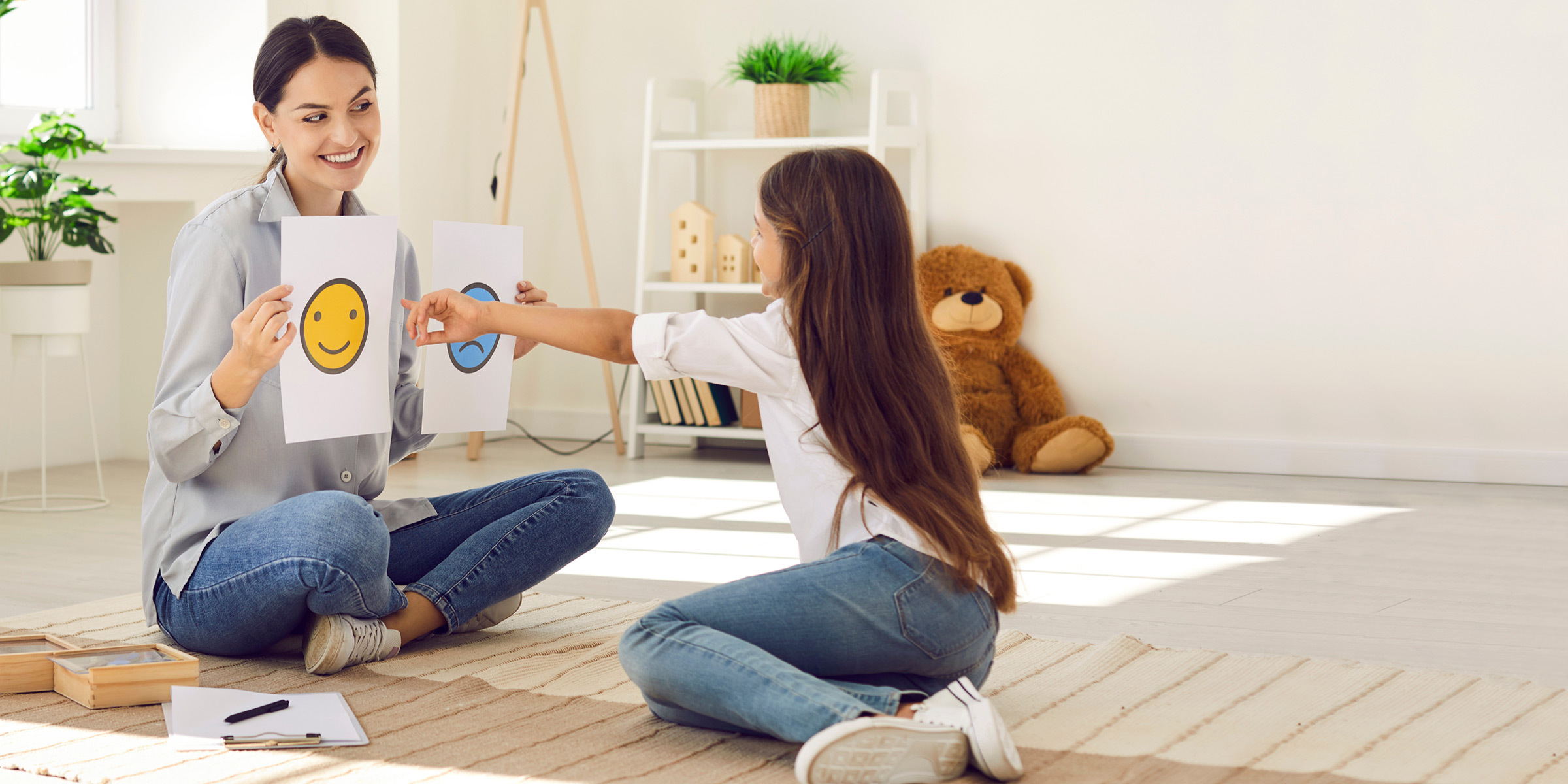 Girl pointing at a happy smiley face on a paper sheet held by educator