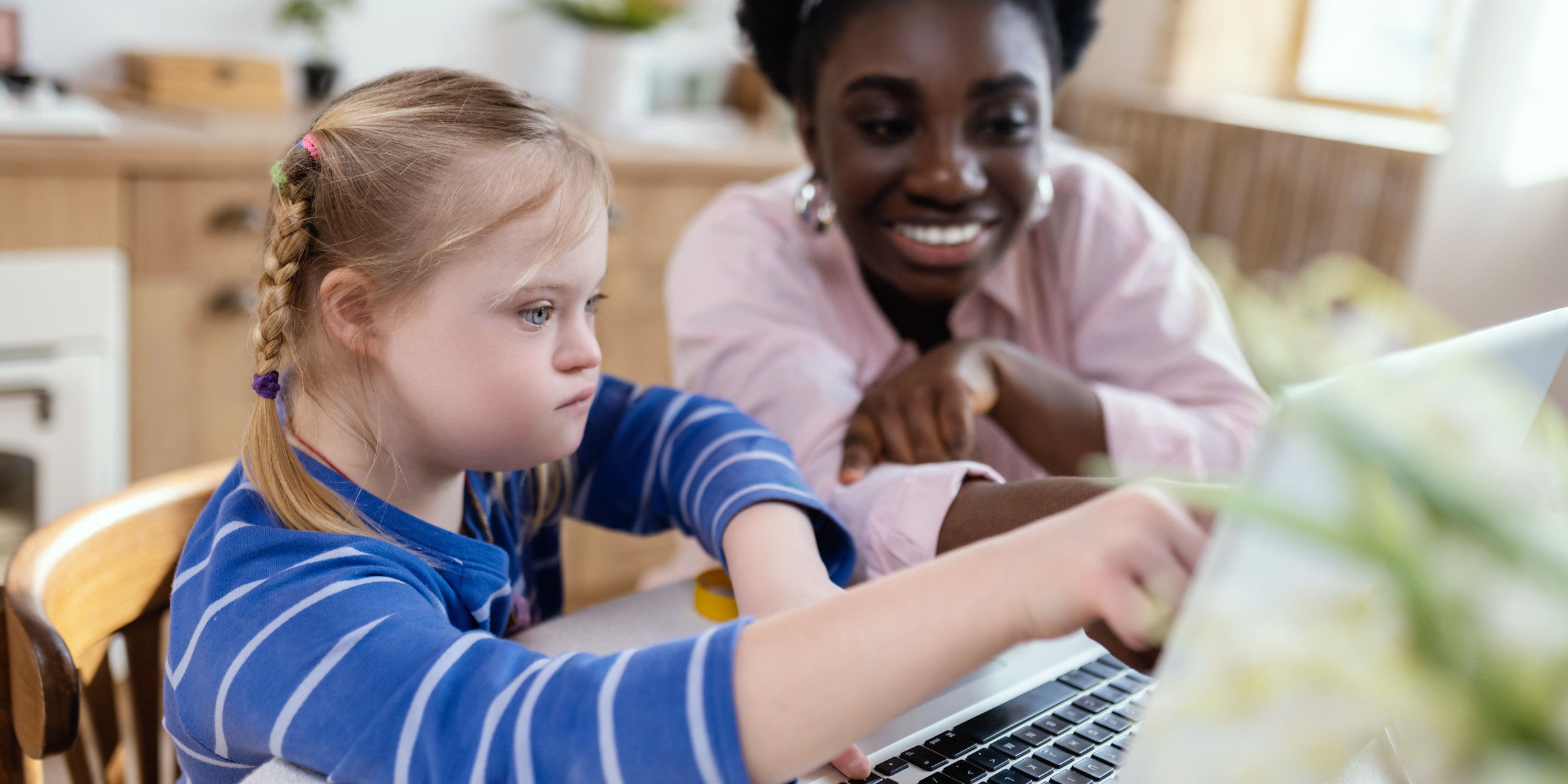 Special needs girl with female teacher pointing at a laptop